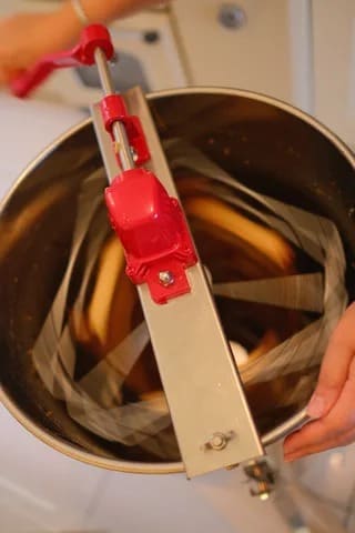 Looking down into the extractor as hands turn the red crank handle, with frames blurred as they spin.